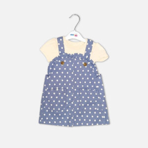 Baby girl 2-piece summer clothing set displaying a denim blue sleeveless pinafore dress with a white polka dot print, front patch pockets, and brown buttons, layered over a short-sleeve cream inner bodysuit from Mini & Me.