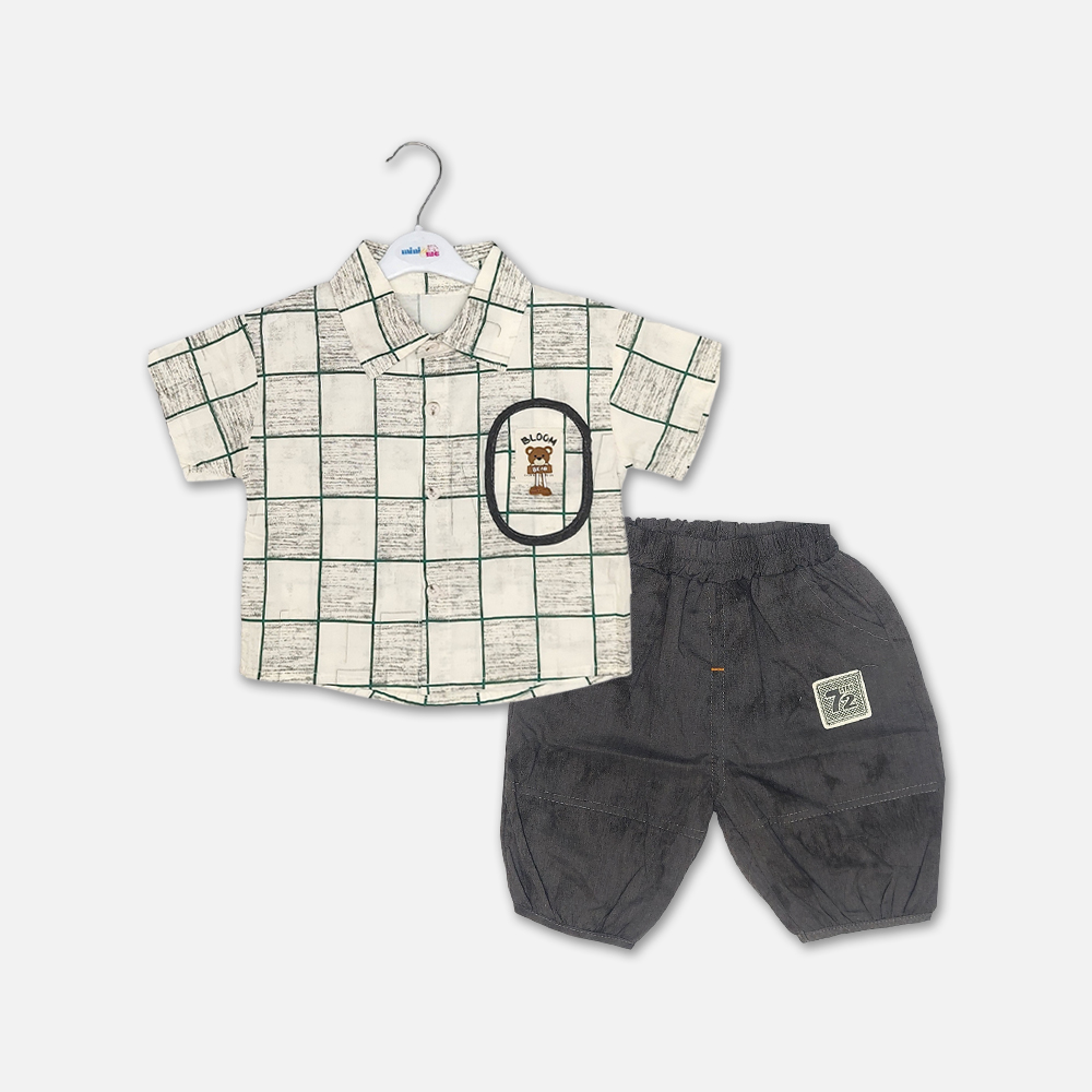 20-1 Mini and Me boys two piece summer suit set hanging on a white hanger, featuring a cream short sleeve button down shirt with a green checkered grid pattern and a cartoon bear chest pocket graphic, paired with matching textured charcoal grey shorts featuring a small square number patch, displayed on a light gray background in file 20-1_2.jpg.