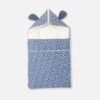 A premium newborn convertible carry nest sleeping bag featuring a blue exterior print with white stars and paw prints, a soft off-white cushioned interior, and a convertible zippered hood accented with cute dark blue 3D ears.