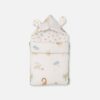 A convertible cream-colored baby carry nest featuring a pastel safari animal print with elephants, giraffes, and lions, showing both the open rectangular bedding layout and the zipped hooded setup with fabric ears.