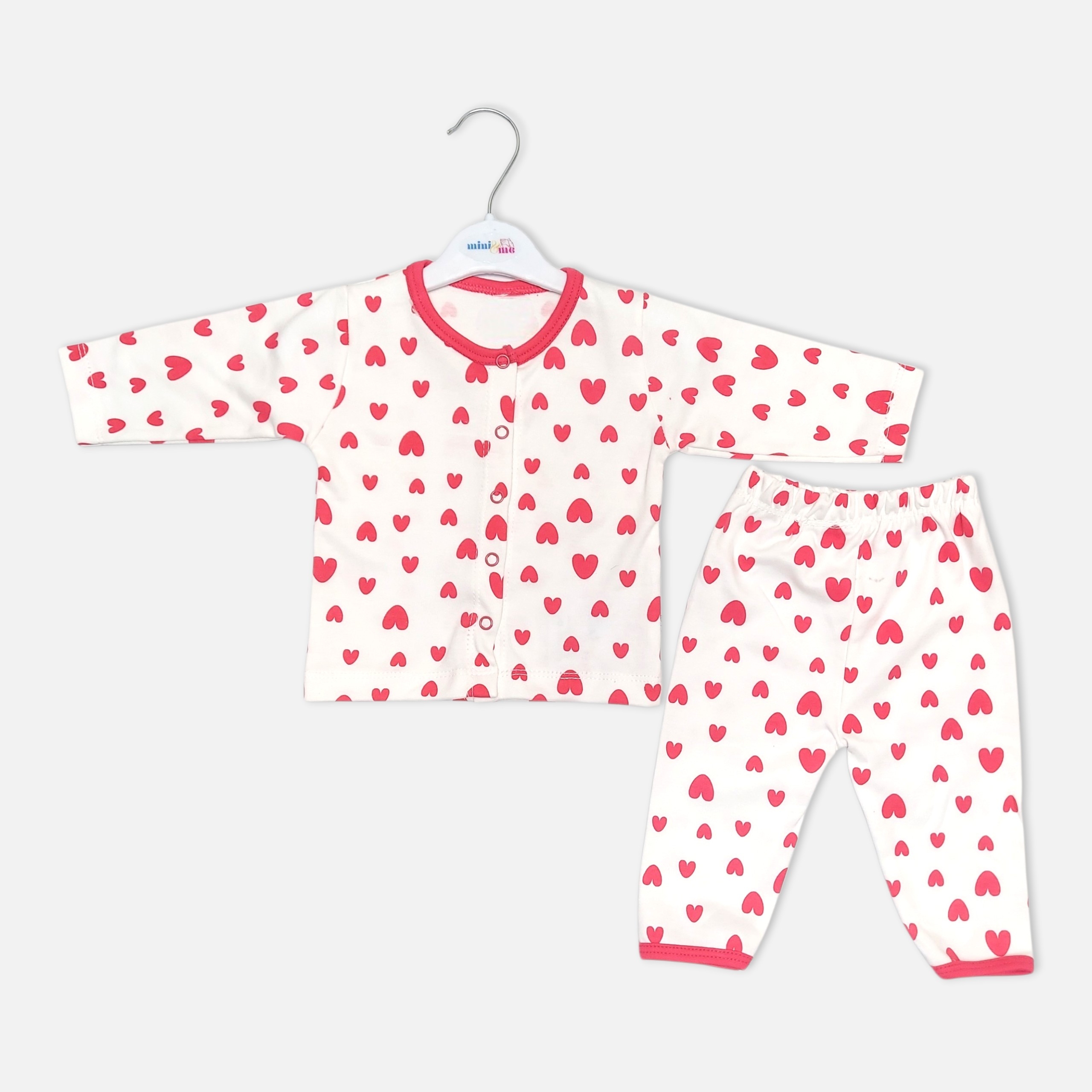 20260713_192138 (9) Unisex white cotton baby sleepwear set featuring a long-sleeve button-up top and matching pull-on pants decorated with an all-over pink heart print and pink trim.