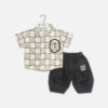 Mini and Me boys two piece summer suit set hanging on a white hanger, featuring a cream short sleeve button down shirt with a green checkered grid pattern and a cartoon bear chest pocket graphic, paired with matching textured charcoal grey shorts featuring a small square number patch, displayed on a light gray background in file 20-1.jpg.