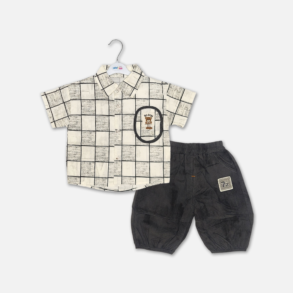 21-1 Mini and Me boys two piece summer suit set hanging on a white hanger, featuring a cream short sleeve button down shirt with a green checkered grid pattern and a cartoon bear chest pocket graphic, paired with matching textured charcoal grey shorts featuring a small square number patch, displayed on a light gray background in file 20-1.jpg.