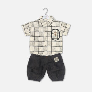 Mini and Me boys two piece summer suit set hanging on a white hanger, featuring a cream short sleeve button down shirt with a green checkered grid pattern and a cartoon bear chest pocket graphic, paired with matching textured charcoal grey shorts featuring a small square number patch, displayed on a light gray background in file 20-1.jpg.