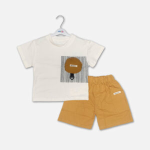 Mini and Me boys two piece summer casual suit set hanging on a white hanger, featuring a cream short sleeve crewneck t-shirt with a black typographic block print and a decorative brown circular pouch, paired with matching mustard yellow cotton shorts with an elastic waist, displayed on a light gray background.