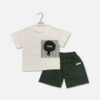Mini and Me boys two piece summer suit set hanging on a white hanger, featuring a white short sleeve t-shirt with a black studio typography square block and a circular dark olive green pouch pocket, paired with matching olive green cargo shorts with an elastic waist, displayed on a clean light gray background.