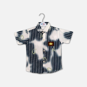 A boys short sleeve button down shirt hanging on a white hanger, featuring a graphic print of vertical navy blue stripes mixed with white tie-dye patches, scattered light green alphabet letters, and a small brown square leather chest patch, displayed over a light gray background.
