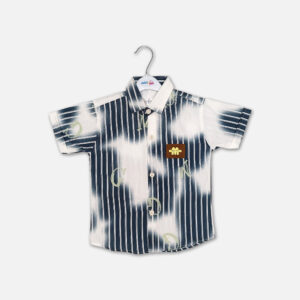 Mini and Me boys short sleeve button down shirt hanging on a white hanger, featuring a navy blue and white vertical striped pattern fused with large white tie dye cloud washes, an overlay of faint green letters, a structured collar, and a square brown faux leather chest patch, displayed on a light gray background.
