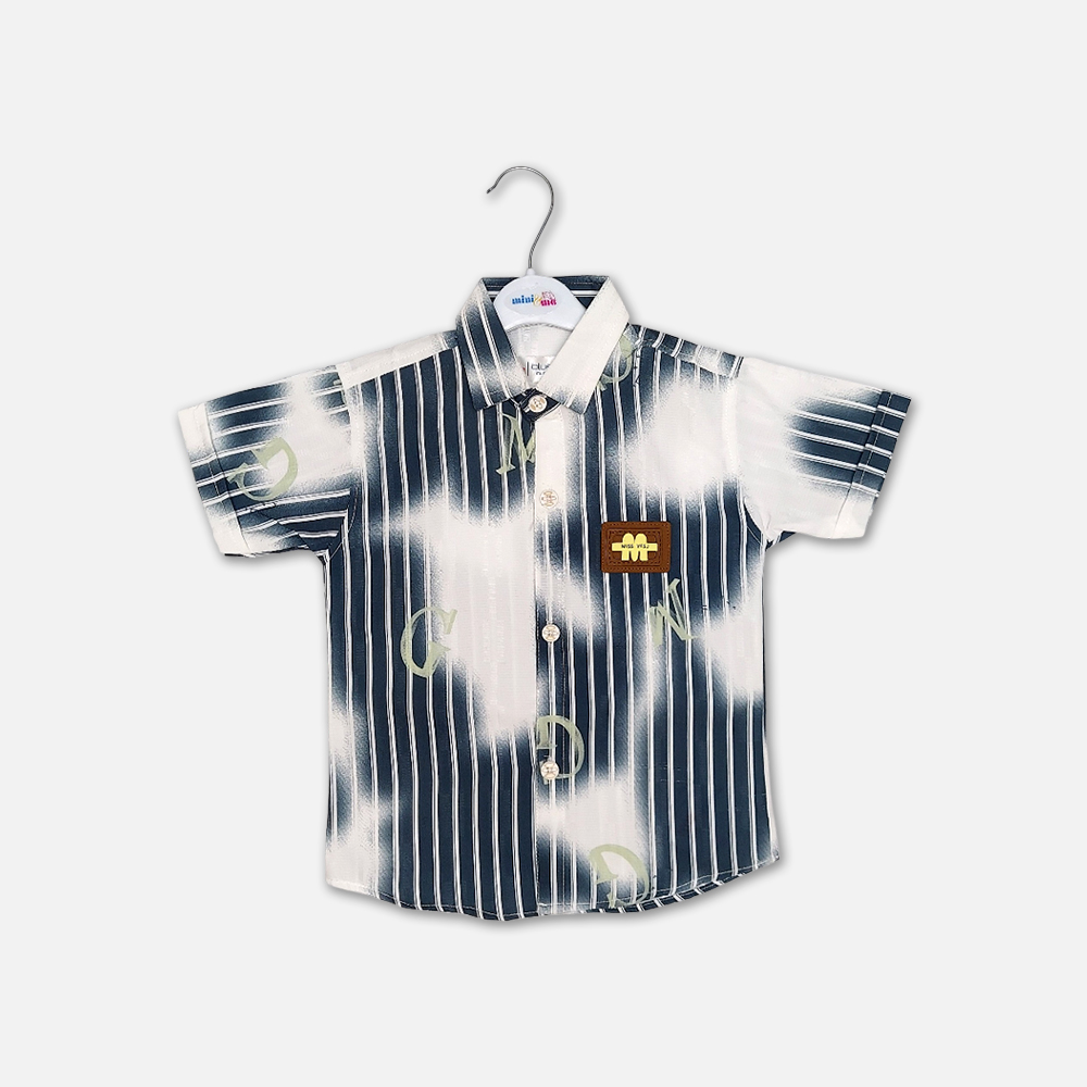 24-1 Mini and Me boys short sleeve button down shirt hanging on a white hanger, featuring a navy blue and white vertical striped pattern fused with large white tie dye cloud washes, an overlay of faint green letters, a structured collar, and a square brown faux leather chest patch, displayed on a light gray background.