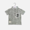 Alt Text Light olive-gray textured short-sleeve polo shirt for toddler boys featuring a black three-button collar, a front chest pocket with a graphic design, and casual stitched patches, displayed on a hanger.