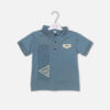 A toddler boys' short-sleeve polo shirt in blue-gray, featuring a textured collar with three buttons, a small chest patch, and a vertical text graphic print with a triangle design on the front, hanging on a white hanger.