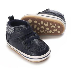 Pair of unisex navy blue faux leather baby sneakers with a secure velcro strap, decorative laces, and a flexible non-slip sole showing a footprint pattern.