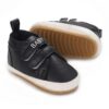 Black leather baby sneakers with white trim and double velcro straps displaying the word baby, showcasing the non-slip tan textured sole.