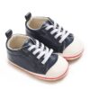 Pair of navy blue faux leather baby sneakers featuring classic white laces, a white rubber-style toe cap, a white sole border with a thin red stripe, and a navy leather heel pull tab.