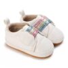 Pair of white faux leather baby pre-walker sneakers featuring a cloud-shaped hook-and-loop strap closure, three sparkling glitter elastic bands in pink, gold, and blue, a soft fabric lining, and a flexible tan-colored soft sole.