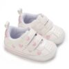 Pair of white faux leather baby pre-walker sneakers featuring embroidered pink hearts on the sides and straps, dual adjustable hook-and-loop straps, a pink heel patch, and a flexible white outsole with a thin pink stripe.