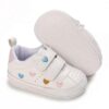 Pair of white faux leather baby pre-walker sneakers featuring embroidered pink, blue, and gold hearts on the sides and straps, dual hook-and-loop straps, a pink heel patch, and a flexible white soft sole embossed with small hearts.