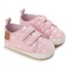 Pair of light pink faux leather baby pre-walker sneakers featuring an all-over white heart print, dual adjustable hook-and-loop straps, a small brown leather-style side tag, and a flexible white soft sole.
