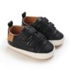 Pair of black textured leather baby sneakers with double hook-and-loop straps, white rubber-look sole border, brown heel accents, and light brown interior lining.