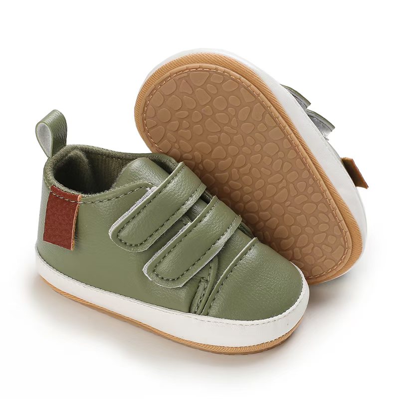 IMG-20260114-WA0121 Olive green leather baby sneakers with a white sole border, double velcro straps, a small brown accent patch, and a textured tan non-slip sole.