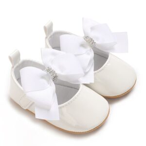 Pair of white patent leather baby Mary Jane pre-walker dress shoes featuring an oversized white grosgrain ribbon bow with a sparkling rhinestone center, a hidden strap closure, and a flexible tan soft sole.