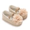 A pair of cream colored infant dress shoes featuring a diamond quilted stitching pattern, a large layered chiffon fabric flower on the toe, and a flexible tan sole on a clean white background.