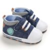 Pair of denim blue canvas high-top baby sneakers featuring a white toe cap, white elastic laces with brown eyelets, a single hook-and-loop strap, a round mint-green side patch, and a blue-and-white striped inner ankle collar.