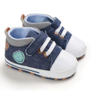 Pair of denim blue canvas high-top baby sneakers featuring a white toe cap, white elastic laces with brown eyelets, a single hook-and-loop strap, a round mint-green side patch, and a blue-and-white striped inner ankle collar.