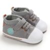 Pair of grey canvas high-top baby sneakers featuring a white protective toe cap, grey elastic laces with brown metal eyelets, a single hook-and-loop strap, a round mint-green side patch, and a grey-and-white striped ankle collar.