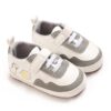 Pair of white faux leather baby pre-walker sneakers with grey accents, white elastic laces, an adjustable strap, a soft grey fabric lining, and a cute cartoon dinosaur graphic with a yellow hello speech bubble on the side.