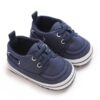 Pair of navy blue canvas baby boat shoes with matching blue elastic laces, silver-tone metal eyelets, a white sole border with a navy stripe, and a canvas heel pull tab.