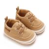 Pair of tan canvas baby boat shoes with matching tan elastic laces, silver-tone metal eyelets, a white sole border with a tan stripe, and a canvas heel pull tab.