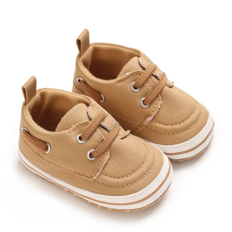 IMG-20260114-WA0169 Pair of tan canvas baby boat shoes with matching tan elastic laces, silver-tone metal eyelets, a white sole border with a tan stripe, and a canvas heel pull tab.