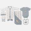 A 7-piece newborn baby starter layette set laid out on a gray background, featuring a white long-sleeve snap romper with a vintage car print, a matching beanie hat, mittens, a rolled white washcloth, a solid blue-gray short-sleeve bodysuit with camper van embroidery, a matching hooded blanket, and a feeding bib.