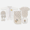 A 7-piece newborn baby starter layette set laid out on a gray background, featuring a white long-sleeve snap romper with grey polka dots, a matching beanie hat with a teddy bear face print, matching mittens, a rolled washcloth, a grey short-sleeve bodysuit, a matching hooded blanket, and a feeding bib with an embroidered teddy bear.