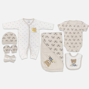 A 7-piece newborn baby starter layette set laid out on a gray background, featuring a white long-sleeve snap romper with grey polka dots, a matching beanie hat with a teddy bear face print, matching mittens, a rolled washcloth, a grey short-sleeve bodysuit, a matching hooded blanket, and a feeding bib with an embroidered teddy bear.