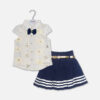 A premium two-piece baby girls clothing set featuring a white cap-sleeve button-down shirt with embroidered flowers, sequins, and a navy bow tie, alongside a pleated navy blue skirt with silver stripes and a metallic gold belt, displayed on a hanger.