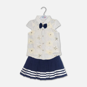 A premium two-piece baby girls clothing set featuring a white cap-sleeve button-down shirt with embroidered flowers, sequins, and a navy bow tie, alongside a pleated navy blue skirt with silver stripes and a metallic gold belt, displayed on a hanger.