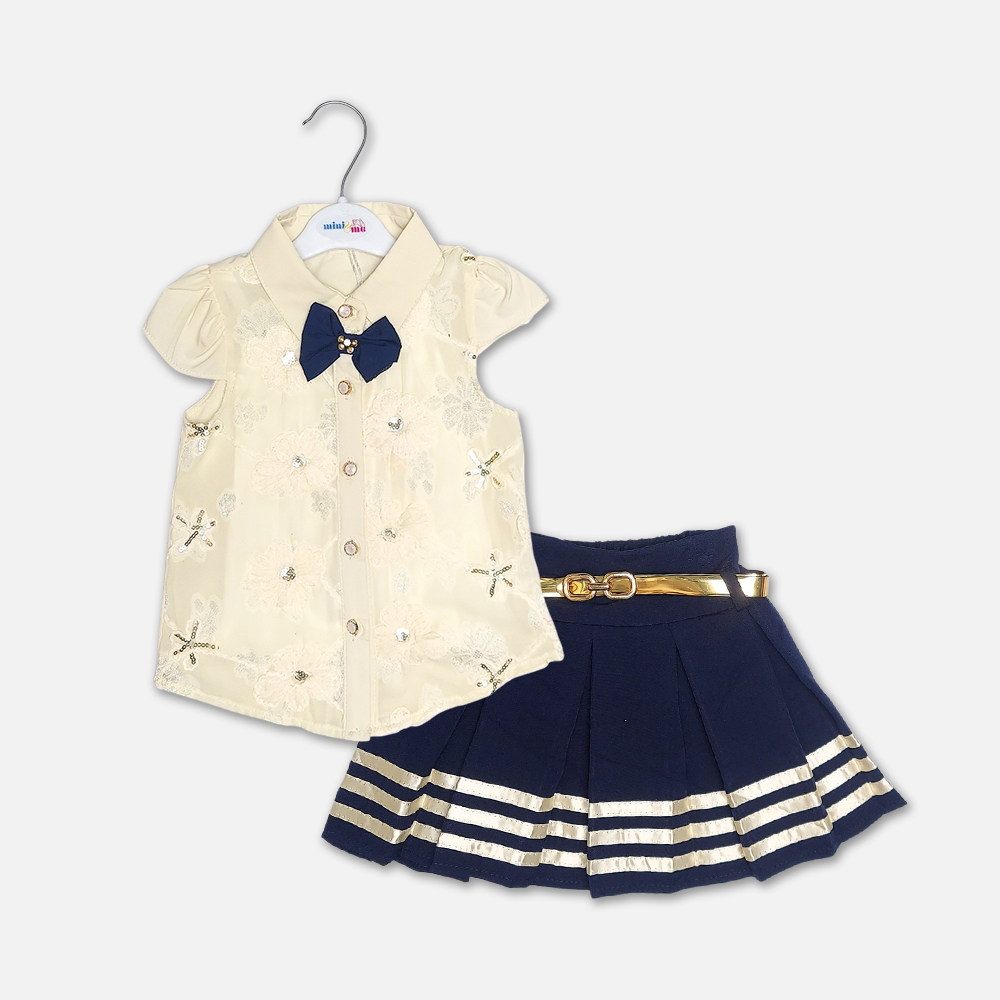 girlsSuit13133-3-1 A premium two-piece baby girls clothing set featuring an off-white cap-sleeve button-down shirt with embroidered flowers, sequins, and a navy bow tie, alongside a pleated navy blue skirt with gold stripes and a metallic gold belt, displayed on a hanger.