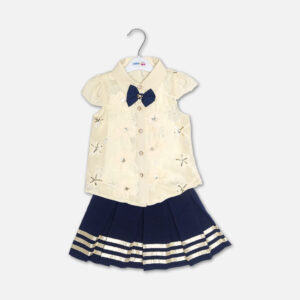 A premium two-piece baby girls clothing set featuring an off-white cap-sleeve button-down shirt with embroidered flowers, sequins, and a navy bow tie, alongside a pleated navy blue skirt with gold stripes and a metallic gold belt, displayed on a hanger.