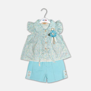 A premium two-piece summer clothing set for baby girls featuring a light blue button-down blouse with an all-over ditsy floral print, ruffle sleeves, and a matching blue fabric flower brooch, alongside sky blue shorts with matching floral side panels, displayed on a hanger.