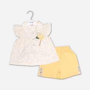 A premium two-piece summer clothing set for baby girls featuring a cream button-down blouse with an all-over ditsy floral print, ruffle sleeves, and a yellow fabric flower brooch, alongside pastel yellow shorts with matching floral side panels, displayed on a hanger.