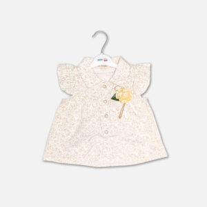 A premium two-piece summer clothing set for baby girls featuring a cream button-down blouse with an all-over ditsy floral print, ruffle sleeves, and a yellow fabric flower brooch, alongside pastel yellow shorts with matching floral side panels, displayed on a hanger.